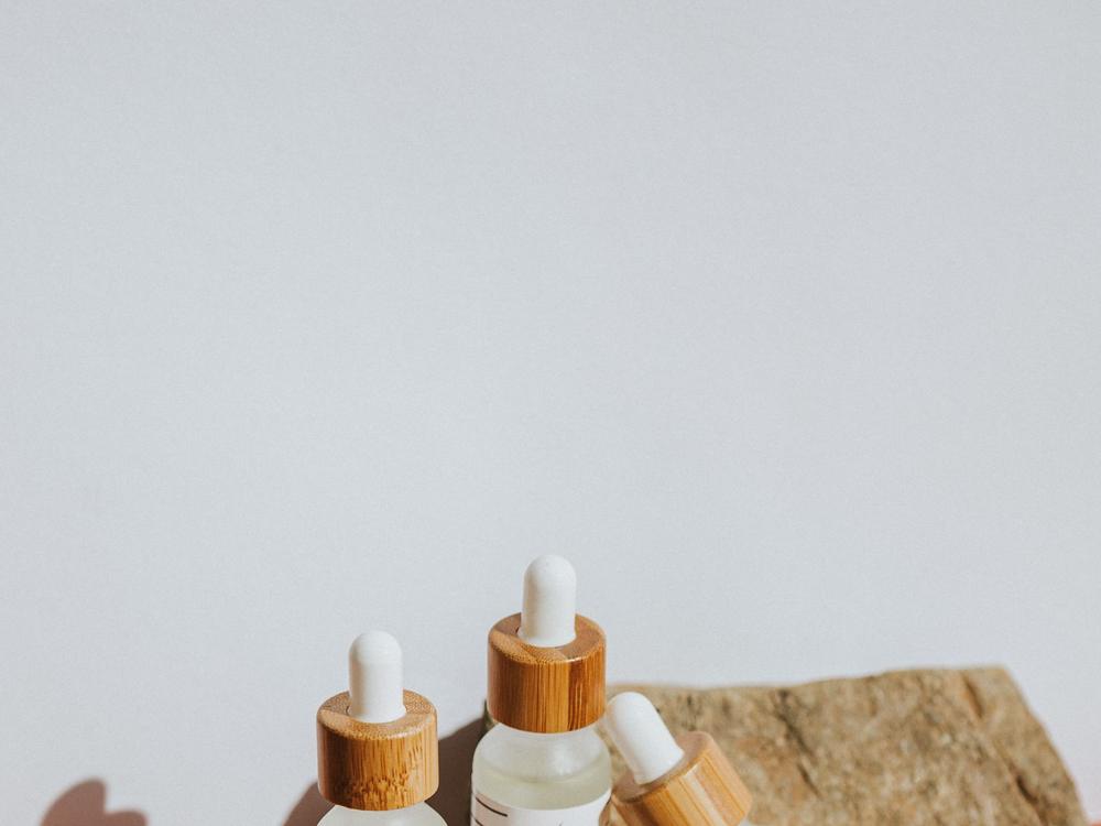 A product shot of skincare droppers arranged with a rough stone on a pale ground
