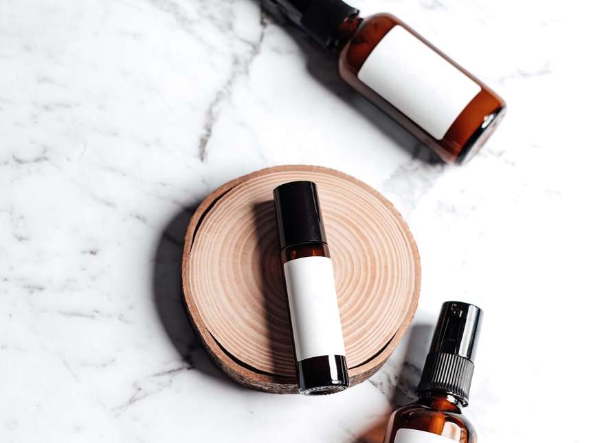 A product shot of brown glass bottles on a marble surface beside a wooden tray
