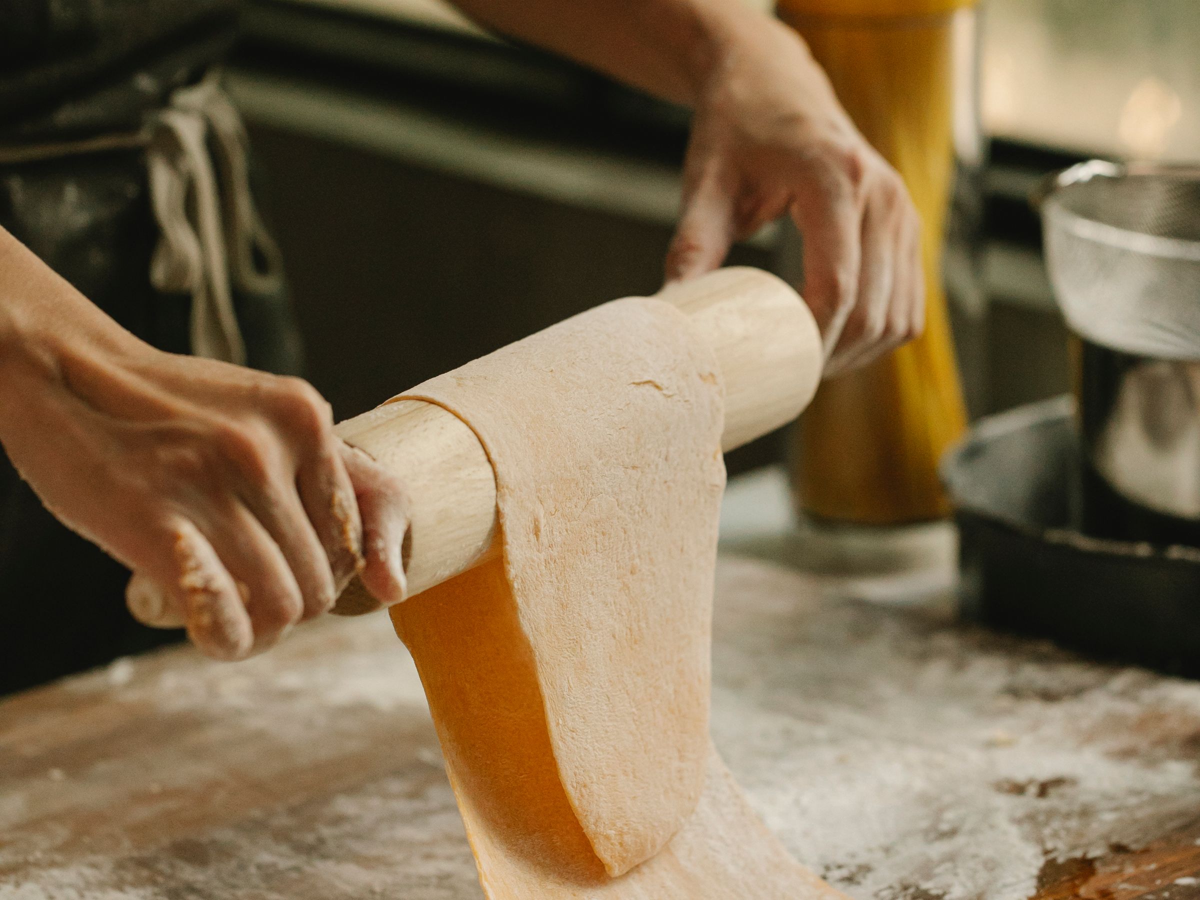 Hands rolling out fresh pasta dough on a floured wooden table